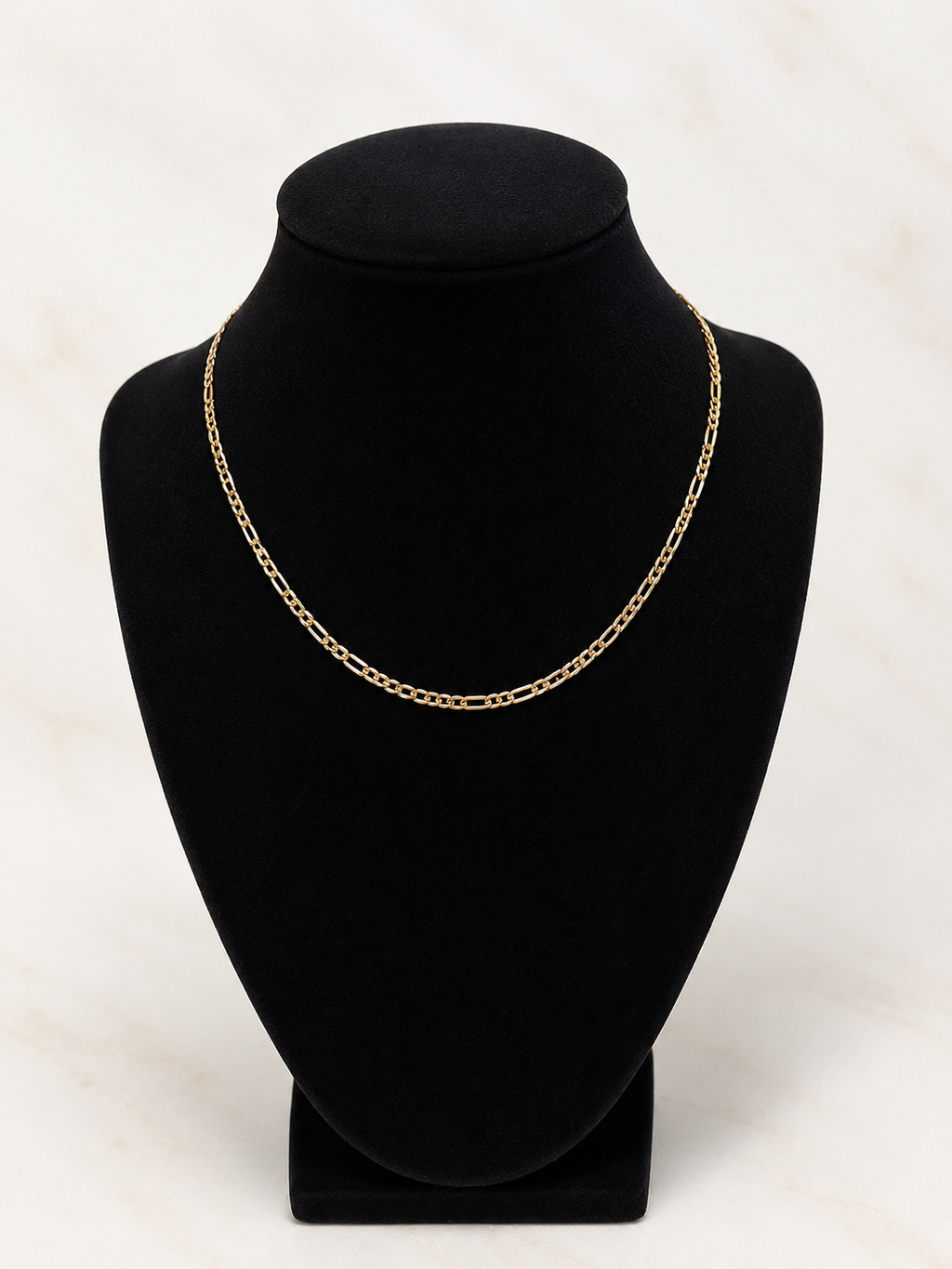 A gold chain necklace displayed on a black velvet jewelry bust against a light marble background.
