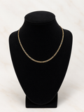 A gold chain necklace displayed on a black velvet jewelry bust against a light marble background.