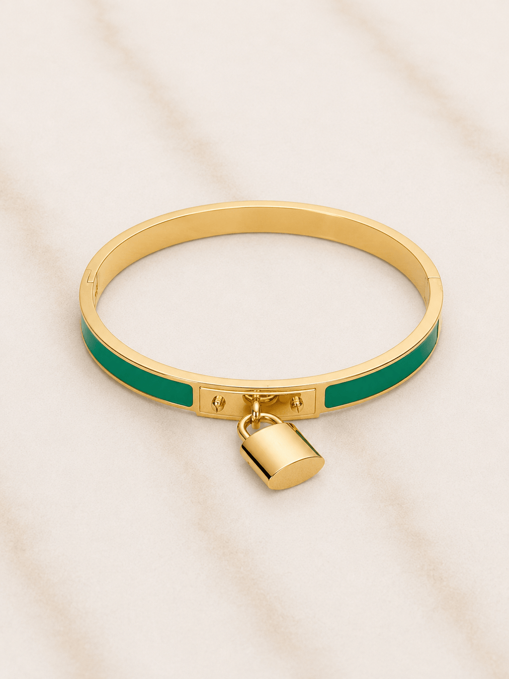 Gold bangle bracelet with a green enamel inlay and a small hanging padlock charm, displayed on a light marble surface.