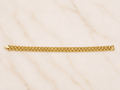 A gold tennis bracelet with a classic curb link design, displayed horizontally on a light beige marble surface.