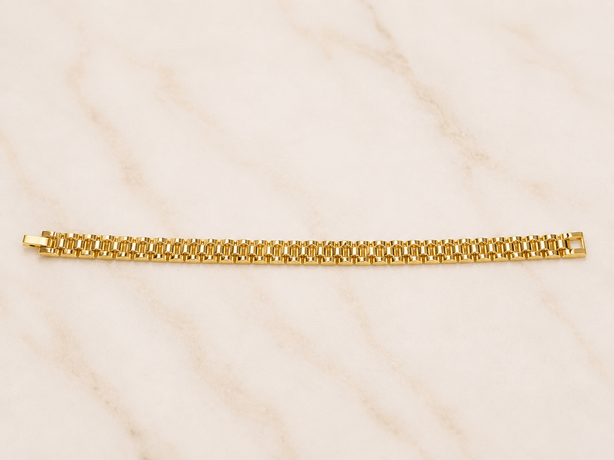 A gold tennis bracelet with a classic curb link design, displayed horizontally on a light beige marble surface.