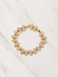A gold-tone floral bracelet with clear pavé stones and small pink gemstone centers, arranged in a circular pattern on a white marble surface.