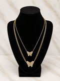 Two layered gold-tone chain necklaces with butterfly pendants, displayed on a black velvet jewelry bust against a light marble-patterned background.