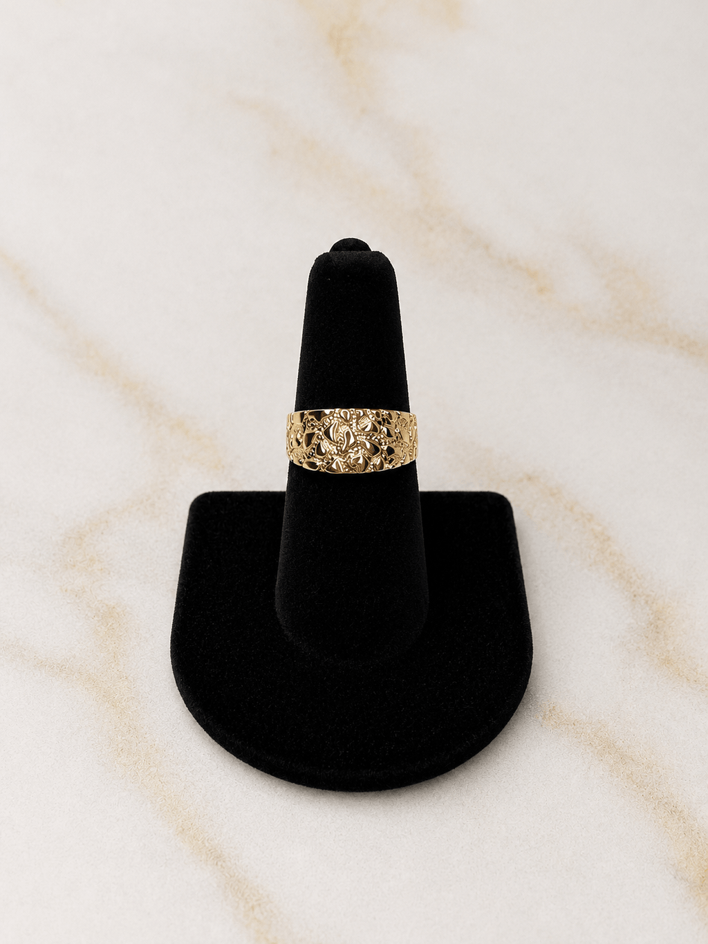 A textured gold ring displayed on a black ring cone stand against a light beige marble background.