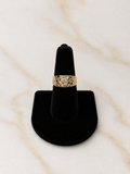 A textured gold ring displayed on a black ring cone stand against a light beige marble background.