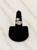 A silver ring with pavé-set clear stones in a leaf-like design, displayed on a black ring stand against a light marble background.