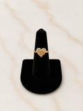 The Reign Golden Heart Ring displayed on a black ring holder, showcasing its unique textured nugget finish and heart accent.