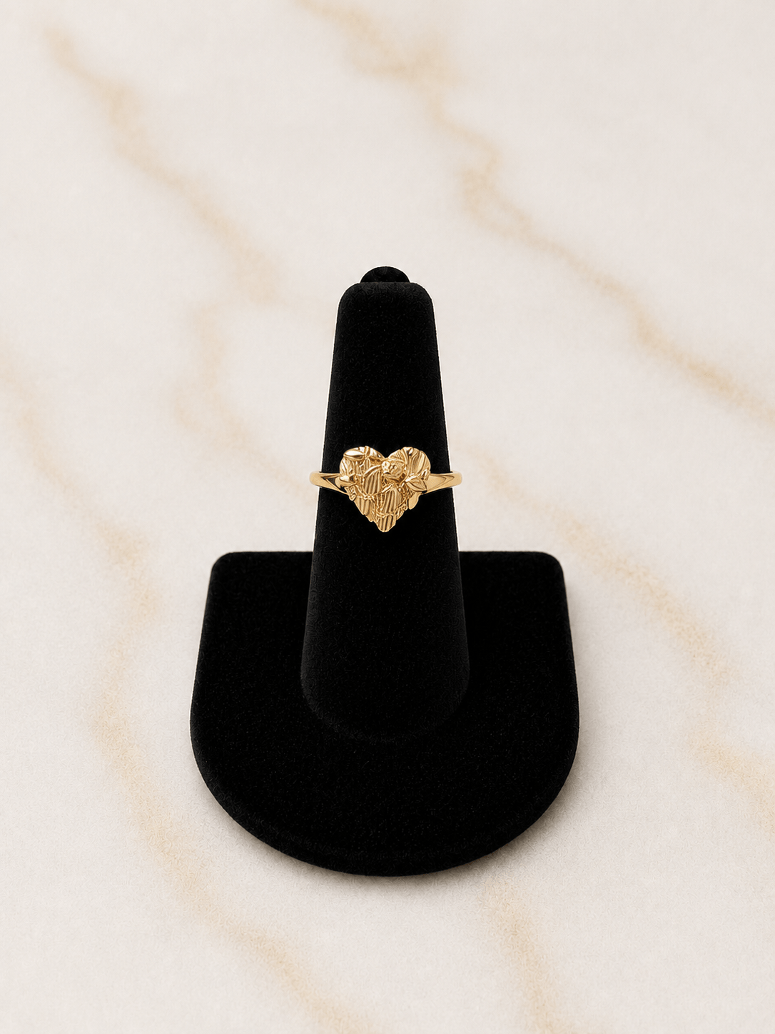 The Reign Golden Heart Ring displayed on a black ring holder, showcasing its unique textured nugget finish and heart accent.