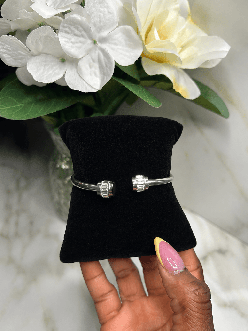 The Royal Radiance Cuff displayed elegantly on a black cushion surrounded by flowers, showcasing its dazzling crystal accents.