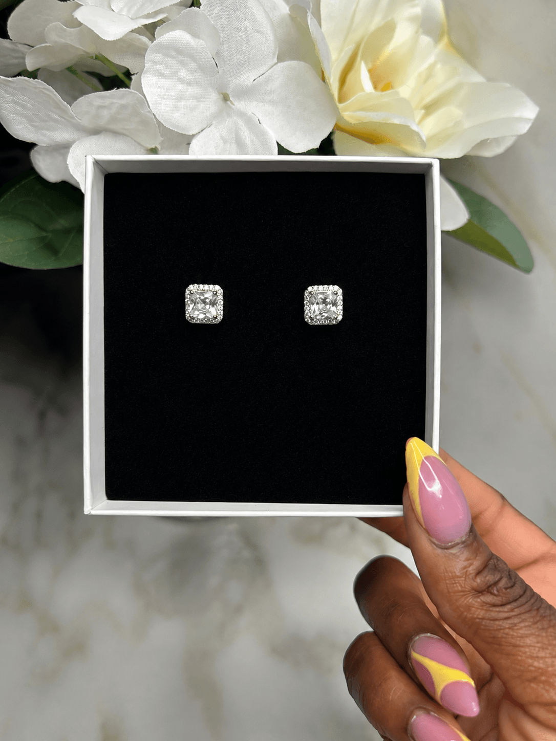 The Reign Diamond Studs displayed in a gift box with floral background, capturing elegance and luxury.