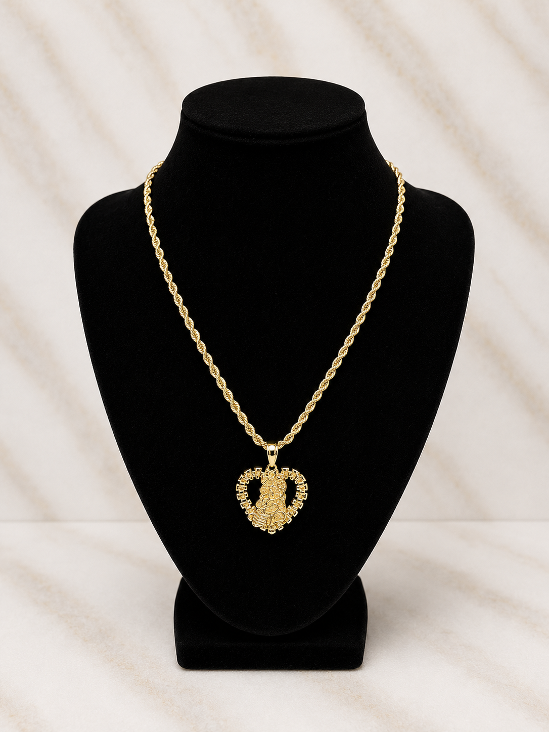 A gold heart-shaped pendant necklace with a textured, pave-like finish, displayed on a black velvet jewelry bust against a light marble-patterned background.