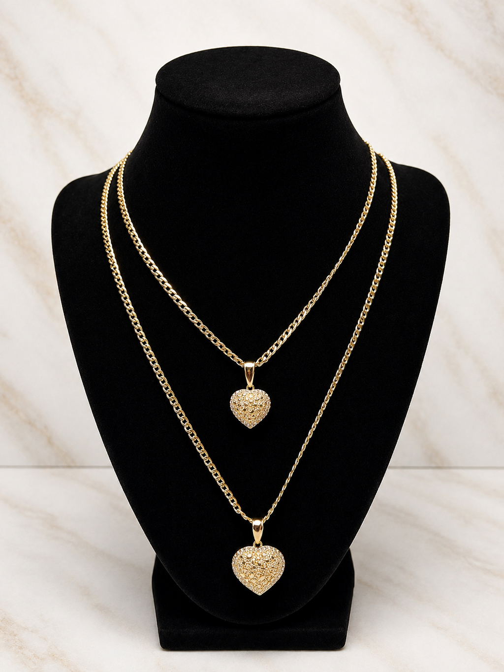 The Royal Heart Bond Necklace displayed on a black bust, featuring two gold chains with heart pendants.