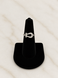 A silver ring with a horseshoe-shaped pavé setting, displayed on a black cone stand against a light marble background.