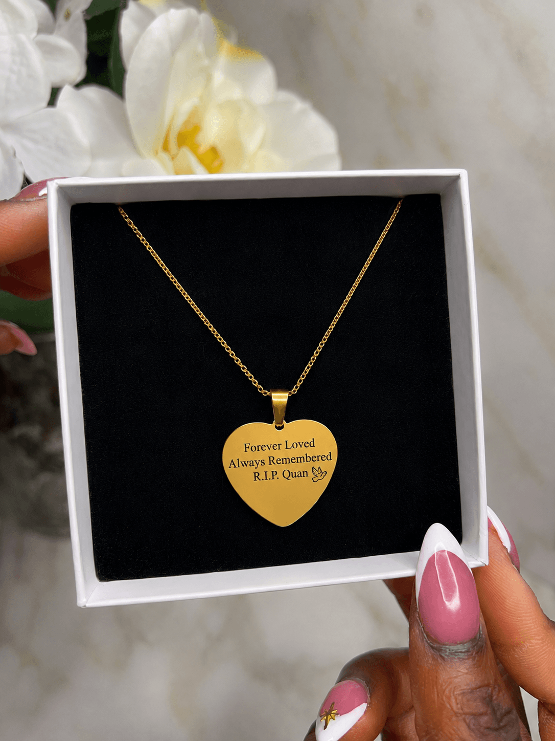 The Royal Heart Necklace displayed in a box, featuring a gold heart pendant with an engraving.