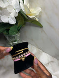 The Royal Heart & Clover Stack jewelry displayed on a black velvet stand with floral background.